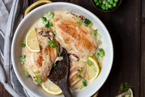 Delizioso pollo al vino bianco in salsa cremosa con broccoli, piselli e fette di limone, guarnito con prezzemolo fresco.