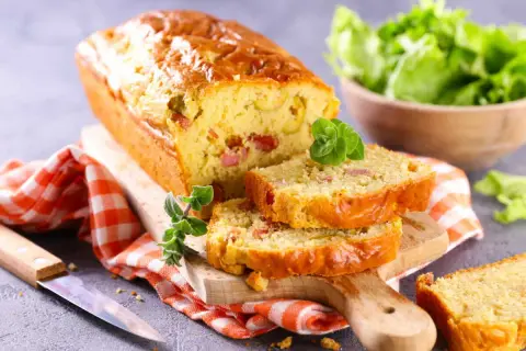 Un cake chorizo poivron, doré et moelleux, coupé en tranches sur une planche en bois. Une salade verte est servie à côté.