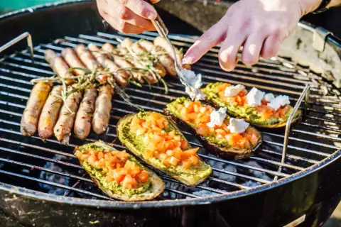 Kiełbaski i bakłażany z pesto i pomidorami pieką się na grillu. Idealne blachy na grilla na letnie popołudnie.