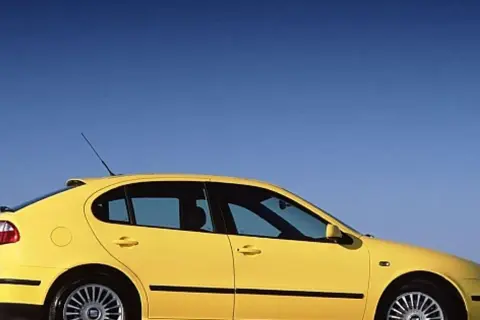 Żółty Seat Leon 2000, sportowy hatchback, zaparkowany na tle błękitnego nieba.