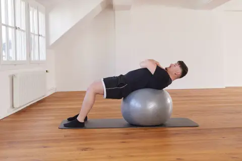 Un homme effectue un exercice avec ballon, le dos courbé sur le ballon de gym, les mains croisées sur la poitrine.
