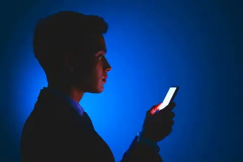 Mężczyzna w garniturze patrzy na jasny ekran telefonu. Dba o ochronę wzroku w telefonie, używając go w ciemności.