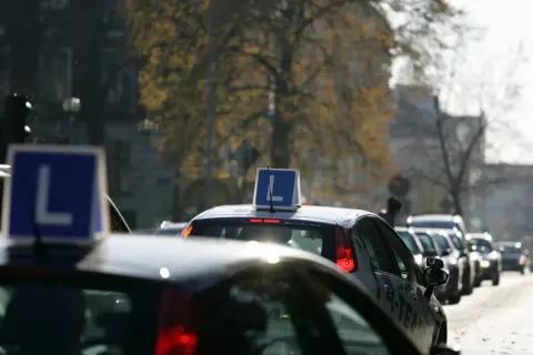 Samochody nauki jazdy z literą "L" na dachu stoją w korku ulicznym.