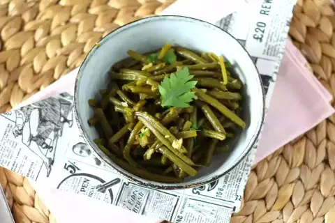 Un tazón de judías verdes salteadas con ajo y perejil, servido sobre un mantel de mimbre.