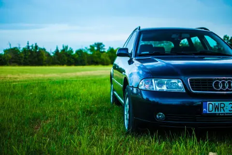 Ciemne Audi A4 B6 2.0 benzyna na tle zielonej łąki i błękitnego nieba.