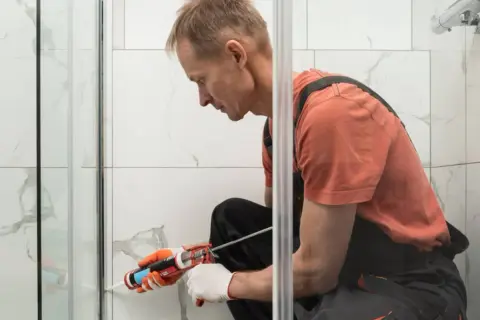 Hombre con guantes aplica sellador para plato de ducha.