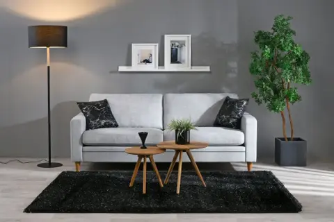 Grå soffa med svarta marmorkuddar, två runda träbord, svart matta och golvlampa i modern stil.