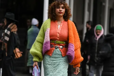 Bunte Strickjacke kombinieren: Ein Outfit mit Strickjacke in Orange, Grün und Lila, dazu ein gemusterter Rock und ein grüner Gürtel.