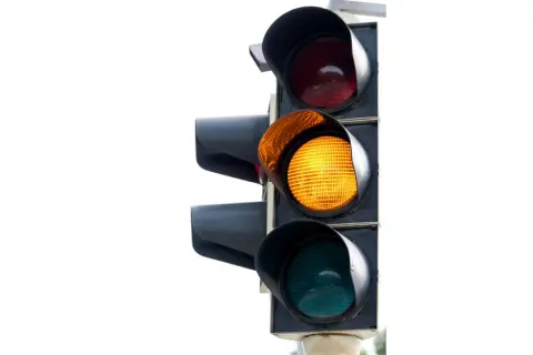 Un feu de circulation avec le voyant orange allumé. Le feu rouge est au-dessus, le vert en dessous.