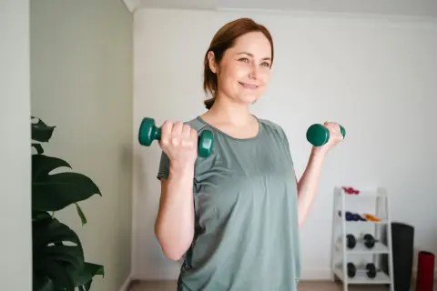 Lächelnde Frau macht Krafttraining mit Hanteln. Sie ist auf dem Weg zum Abnehmen und fühlt sich gut.