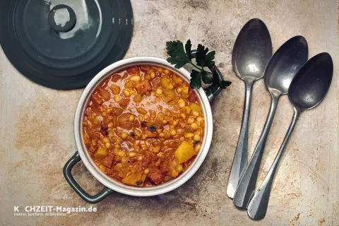 Herzhaftes Bohneneintopf Rezept mit Speck und Kartoffeln, garniert mit Petersilie. Daneben liegen drei Löffel bereit.