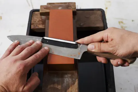 Händer slipar en kniv mot en orange sten. En vass kniv är viktig för matlagning.