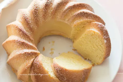 Una soffice torta di ricotta, spolverata di zucchero a velo, con una fetta tagliata che ne rivela la morbidezza.