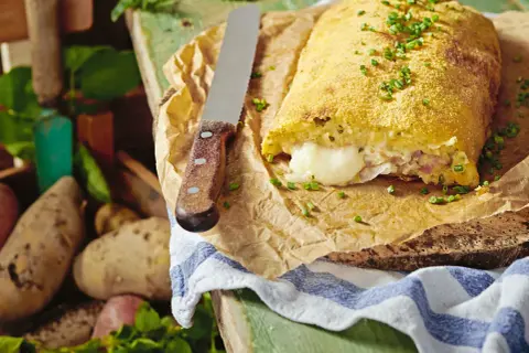 Herzhaft gefüllte polpette di patate, goldbraun paniert, mit geschmolzenem Käse im Inneren. Frische Kartoffeln liegen daneben.