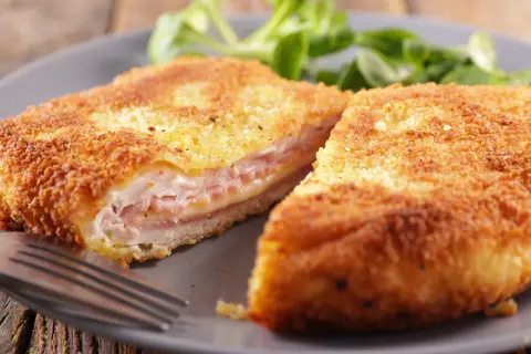 Cotoletta alla valdostana dorata e croccante, farcita con prosciutto e formaggio filante, servita su un piatto grigio con un contorno di insalata verde.