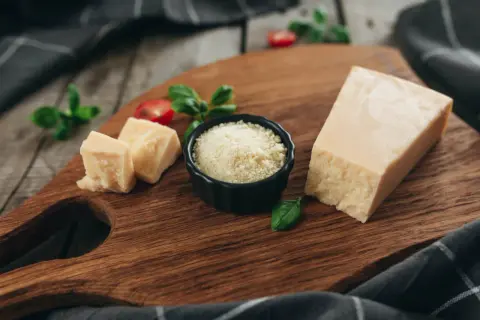 Kawałek parmezanu, pokrojony ser i starty ser do carbonary na drewnianej desce, ozdobione bazylią i pomidorkami.