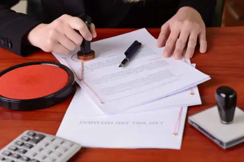 Osoba stempluje dokument, który wygląda jak oświadczenie o dobrowolnym poddaniu się egzekucji. Obok znajduje się poduszka z tuszem i długopis.