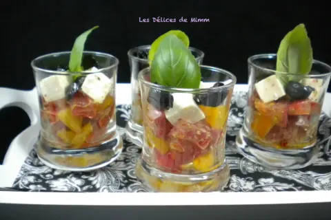 Quatre verrines apéro colorées avec tomates, olives, feta et basilic, présentées sur un plateau décoré.