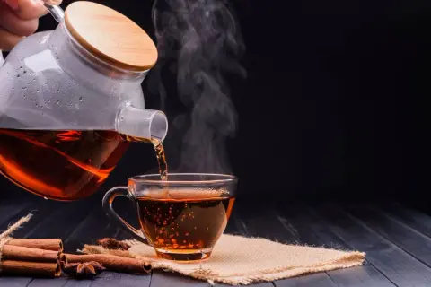 Un thé noir fumant est versé d'une théière en verre dans une tasse. Parfait pour un thé noir le soir, avec des bâtons de cannelle et de l'anis étoilé.