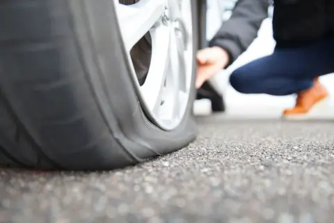 Pneu crevé que faire ? Une personne accroupie examine un pneu à plat sur la route.