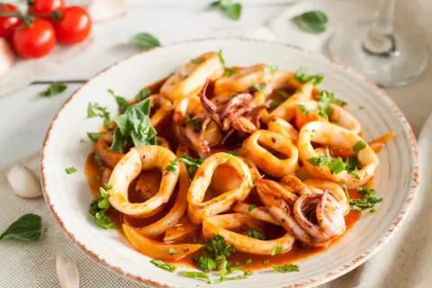 Délicieuse recette encornet à la sauce tomate, garnie de persil frais. Des tomates cerises et de l'ail sont disposés sur le côté.