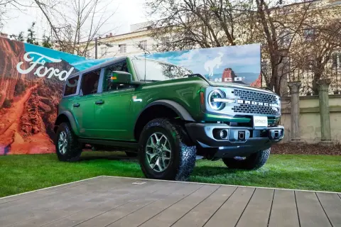 Zielony Ford Bronco prezentuje się imponująco na tle krajobrazu z pustynią i logo Ford.