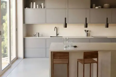 Élégante cuisine couleur taupe, avec des meubles bas et hauts épurés, un îlot central et des tabourets en bois.
