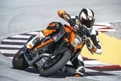 Motocyklista w kombinezonie pochyla się na torze wyścigowym na pomarańczowym motocyklu KTM Super Duke.