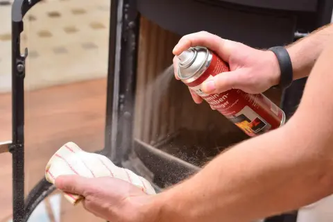 Hände reinigen den Kamin: Mit einem Reiniger wird der Ruß vom Schamottstein und Glas entfernt.