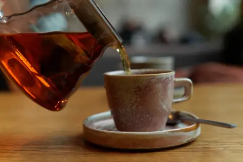 Ciemna czarna herbata nalewana do filiżanki. Osoby z refluksem powinny uważać na ten napój.