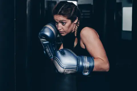 Focused boxer in blue gloves, ready to spar. She looks determined, like a light heavyweight facing a cruiserweight challenge.