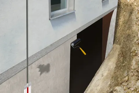 Aplicación de rodillo para impermeabilizar muros enterrados. Se ve la protección de la pared y la tierra excavada.
