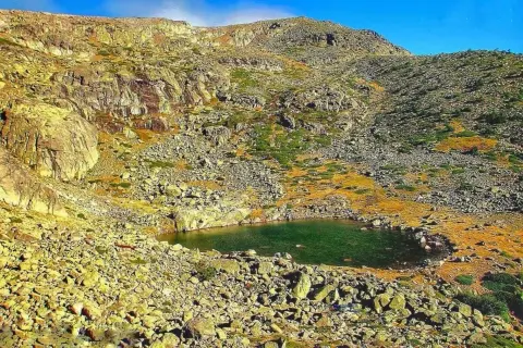 Laguna en la ruta de Peñalara, rodeada de rocas y vegetación de montaña bajo un cielo azul.