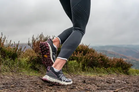 Gambe di una runner su un sentiero fangoso, con erica e colline sullo sfondo. Perfetto per chi vuole iniziare il trail running.
