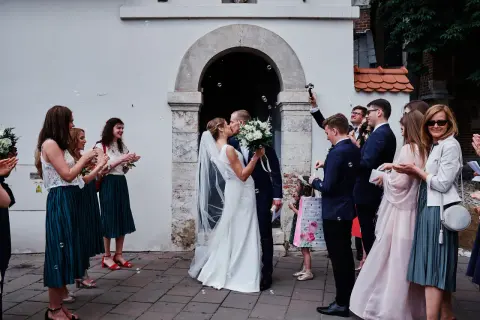 Para młoda całuje się przed kościołem, goście sypią bańki. To piękny ślub kościelny jednostronny.