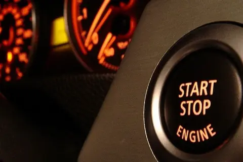 Bouton "START STOP ENGINE" illuminé, prêt à démarrer ou arrêter le moteur. Les cadrans du tableau de bord brillent en orange.