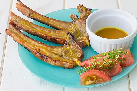 Chuletas de cordero al horno, doradas y jugosas, servidas con una salsa dorada, rodajas de tomate y ramitas de tomillo fresco.