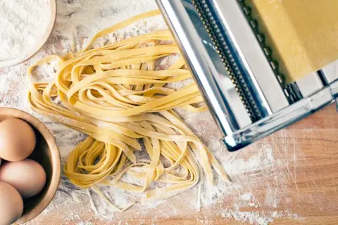 Frischer Tagliatelle-Nudelteig mit Eiern, Mehl und Nudelmaschine auf Holzbrett.