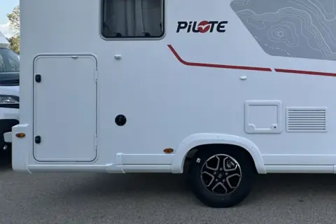 Autocaravanas con garaje, listas para la aventura. Detalle lateral de una autocaravana blanca con puerta de acceso y detalles gráficos.