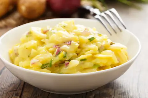 Schüssel mit cremigem Kartoffelsalat, garniert mit Schnittlauch und roten Zwiebeln. Perfekt für 7 Tassen Salat.