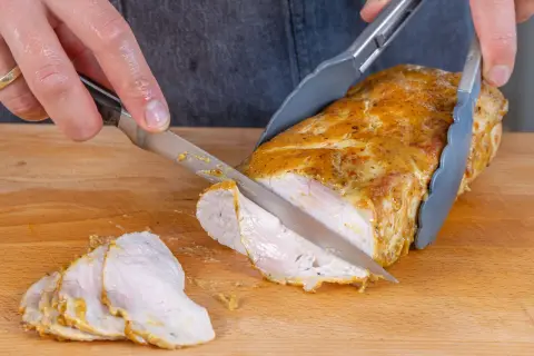 Ein saftiger Schweinelachs wird auf einem Holzbrett in Scheiben geschnitten. Die goldbraune Kruste und das zarte Fleisch sind gut sichtbar.