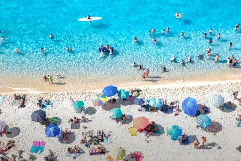 Viste aeree di spiagge di sabbia con fondale basso in Calabria, con bagnanti che si godono il sole e il mare cristallino.