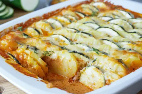 Herzhafter Zucchini Auflauf mit Kartoffeln und geschmolzenem Käse, garniert mit frischen Kräutern.