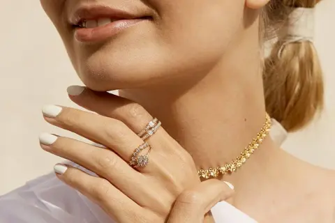 Manos con manicura blanca luciendo dos anillos de **joyería Suárez anillos** y un collar dorado.