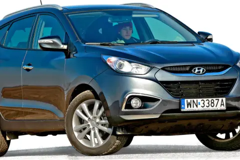 Ciemnoszary Hyundai Tucson, jeden z popularnych koreańskich samochodów, z kierowcą w czerwonej czapce za kierownicą.