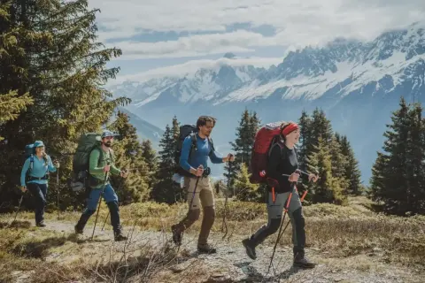 Cuatro personas con mochilas grandes caminan por un sendero montañoso. La diferencia entre senderismo y montañismo se ve en su equipo y el terreno.