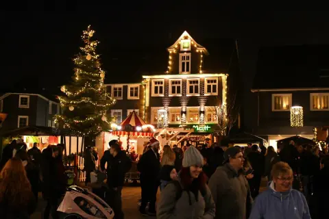 Menschen genießen den stimmungsvollen Radevormwald Weihnachtsmarkt mit beleuchtetem Baum und festlich geschmückten Häusern.