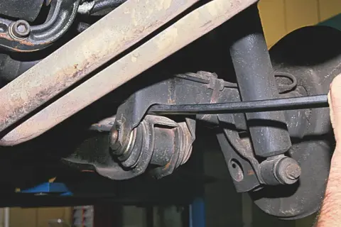 Mechanik pracuje przy wahaczu w samochodzie, używając narzędzia do regulacji.