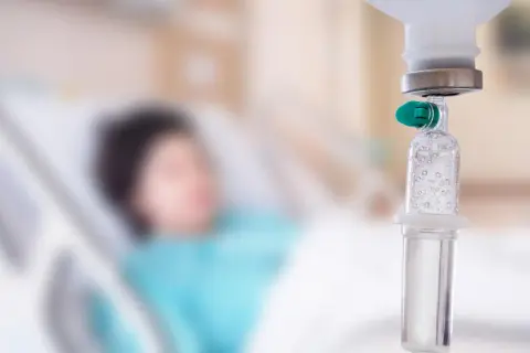 Pacjent w szpitalu otrzymuje kroplówkę. W tle widać łóżko szpitalne. Skutki uboczne nóż gamma mogą być poważne.