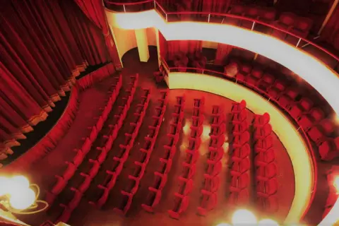Interno del teatro cometa off, con file di poltrone rosse vuote e tende di velluto.
